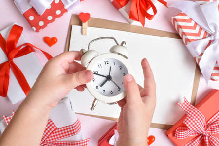 Children's hands hold a white watch on the background of gifts. Flat layout, top view, a place to copy.の写真素材