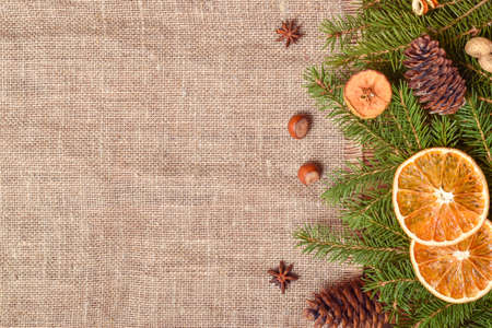 New Year's eco-composition with fir branches, dried oranges, nuts and cinnamon sticks, lying on natural fabric. A mock-up of a Christmas greeting. Copy space. Flat lay, top view.の写真素材