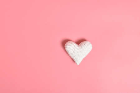 One white knitted heart lies on a pink background in the center. Background for Valentines Day.