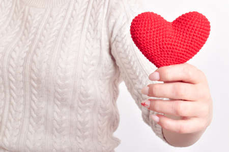 The girl holds a red knitted heart in front of her with one hand. Pregnancy. Banner for Valentine's Day. copyspace.の写真素材