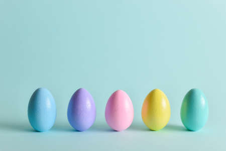 Painted eggs of delicate tones stand on a pale blue background. The minimum composition of Easter. A holiday card with eggs. copy spaceの写真素材