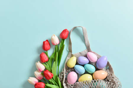 A beautiful bouquet of tulips with a string bag containing painted eggs. Banner for the Happy Easter...
