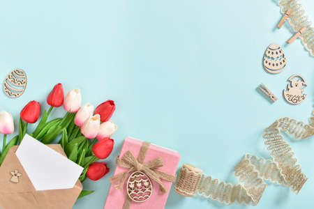 A bouquet of tulips with a postcard and a gift and wooden Easter eggs on a light blue background....