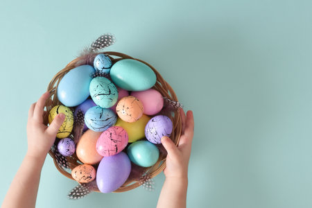Easter card. Minimalism. In the childrens hands is a basket-nest with painted Easter eggs and feathers. Space for copying. Flat position, top view.の写真素材