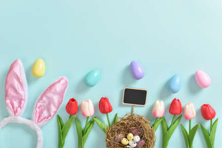 A beautiful bouquet of tulips with a postcard and a gift and a small basket with eggs and feathers on a light blue background.の写真素材