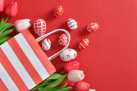 A beautiful bouquet of tulips in a paper eco-bag, with painted Easter eggs on a red background....