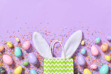 Easter composition with rabbit ears and Easter eggs on a purple background with colored sprinkles....
