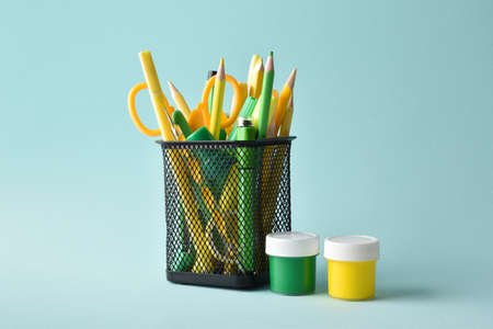 A metal black jar with yellow and green colors and pens and pencils on a light blue background. school supplies. copy spaceの写真素材