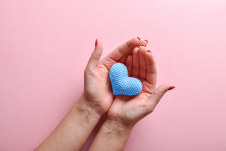 A blue knitted heart in the hands of a girl with a beautiful manicure on a pink backgroundの写真素材