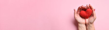 A large horizontal banner with women's hands holding a knitted red heart. Love, mercy, donation.の写真素材