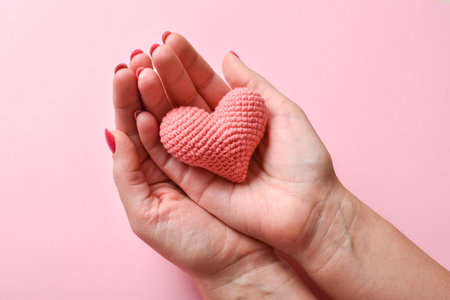 Pink knitted heart in the hands of a girl with a beautiful manicure on a pink background. love....