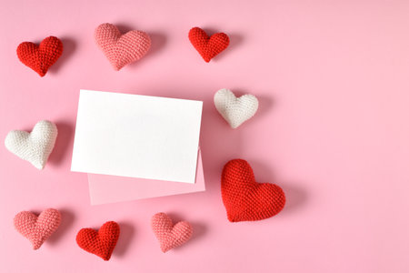 A mock-up of a kraft envelope with a blank sheet and knitted hearts. Valentines Day greeting card with hearts on a pink backgroundの写真素材