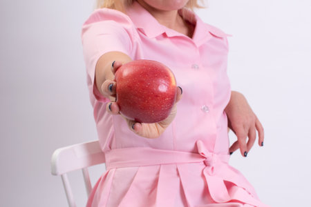 Close-up of a beautician in a pink uniform holding a large red apple.  Space for copying.の写真素材