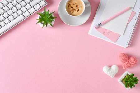 Top view of the office desk. romantic atmosphere. A notebook with a cup of coffee, hearts and a keyboard on a pink background. copyspace. Flat lay, top view.の写真素材