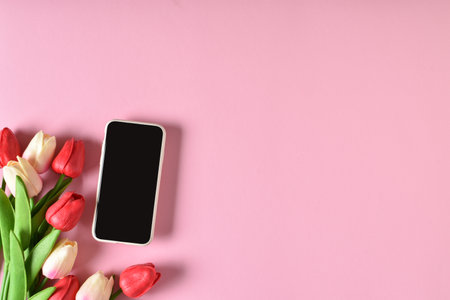A mock-up of a smartphone with tulips and knitted hearts. bloggers and love. Valentine's Day greeting card with hearts on a pink background. copyspace. Flat lay, top view.の写真素材