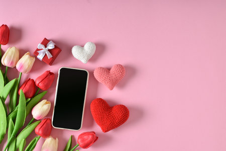 A mock-up of a smartphone with tulips and knitted hearts and a gift . bloggers and love. Valentine's Day greeting card with hearts on a pink background. Space for copying. Flat position, top view.の写真素材