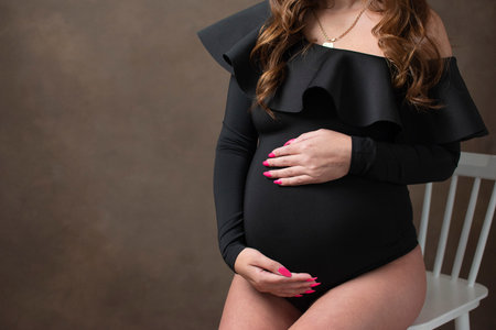 A young girl in a black bodysuit is sitting on a chair with a pregnant belly. Pregnancy and motherhood. copyspace. Flat lay, top view.の写真素材