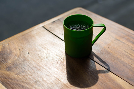 Backlighting photo of Cola in green plastic glass on wooden table with sunset light.の写真素材