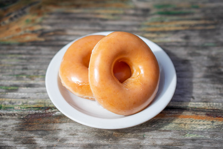 Two delicious donuts on a white dish on wooden table.の写真素材