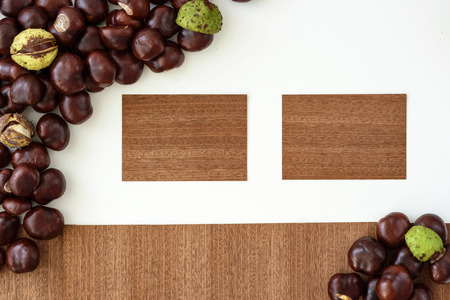 Two wooden cards lying on white table surrounded by freshly harvested chestnuts.