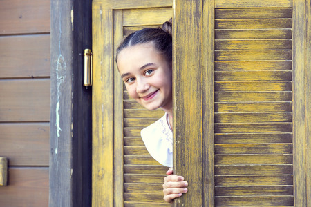 girl looks out from behind a wooden doorの写真素材