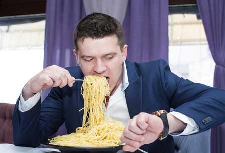 A man in a business suit eating spaghettiの写真素材