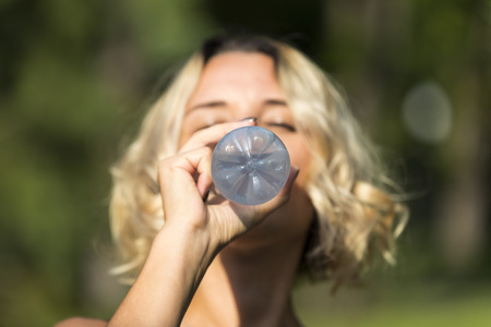 Girl drinks water in a summer park in natureの写真素材