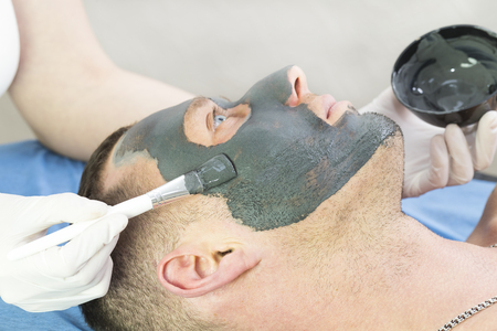 A man does the procedure cleaning his face with a clay mask in the beauty salonの写真素材