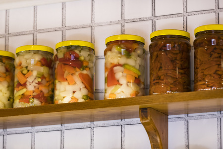 Glass jars with preserving vegetables on wooden shelves.の写真素材