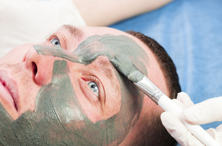 A man does the procedure cleaning his face with a clay mask in the beauty salonの写真素材