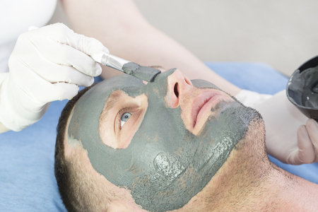 A man does the procedure cleaning his face with a clay mask in the beauty salonの写真素材