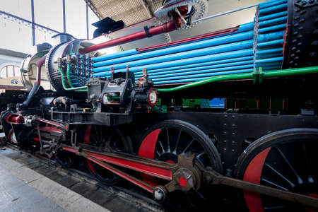 Old steam locomotive with blue and green pipes in the workshop.