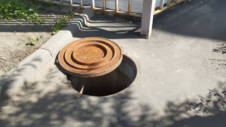 an open hatch on an asphalt road, the rusted lid is pushed to the side