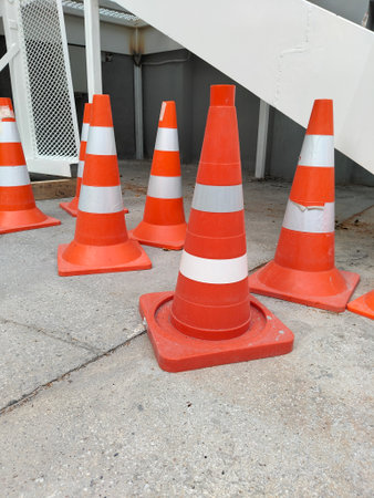 a group of orange and white traffic cones located on a concrete surface under the white metal...
