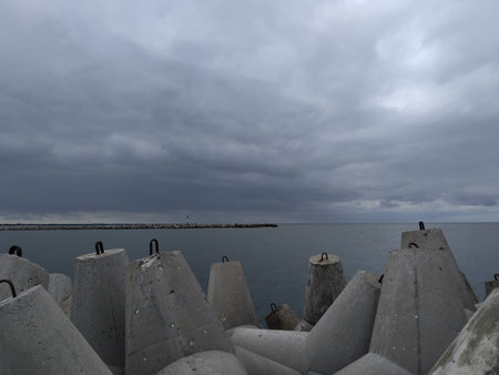 a bleak seascape in gray tones, with concrete breakwaters in the foreground, and a long pier with a small lighthouse in the backgroundの写真素材