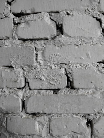 part of a white brick wall with rough uneven bricks of different sizes and uneven seams between them, which are filled with cementの写真素材