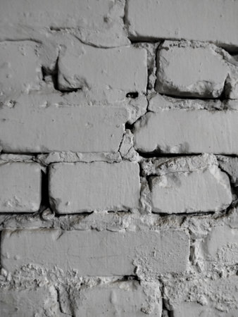 part of a white brick wall with rough uneven bricks of different sizes and uneven seams between...