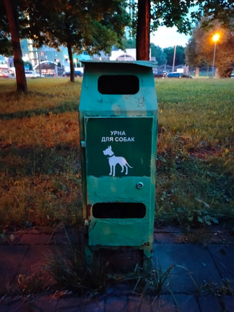 There is a green urn for dog excrement in the evening square.の写真素材
