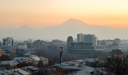 An evening city against a backdrop of large mountains and an orange sunset sky