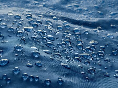 Rain water droplets on blue fiber waterproof fabric. Blue background.の写真素材