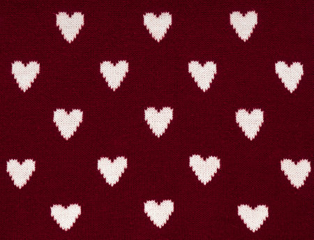 Knitted red background with a white pattern in the shape of heart.