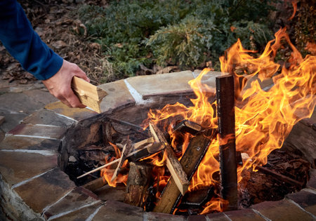 Man touching wooden log while making bonfire near stones
