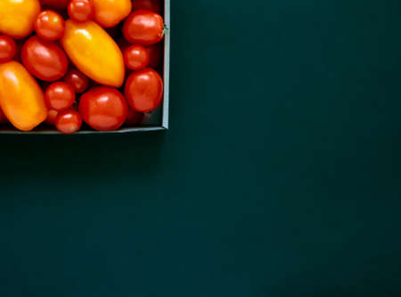 Red and yellow tomatoes in a cardboard box on a dark background with copy space