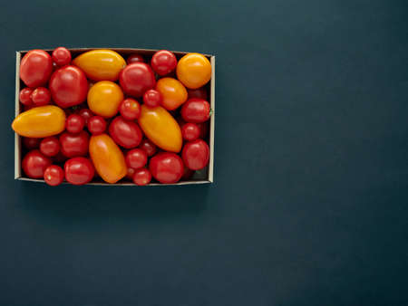 Red and yellow tomatoes in a cardboard box on a dark background with copy spaceの写真素材
