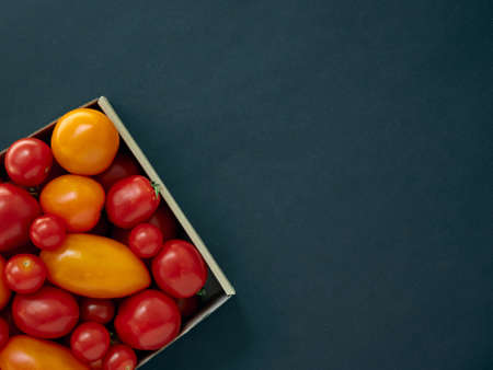 Red and yellow tomatoes in a cardboard box on a dark background with copy spaceの写真素材