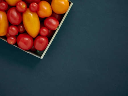 Red and yellow tomatoes in a cardboard box on a dark background with copy spaceの写真素材