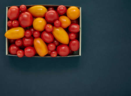Red and yellow tomatoes in a cardboard box on a dark background with copy spaceの写真素材