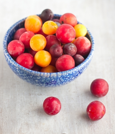 yellow, red, purple plums in the blue bowlの写真素材