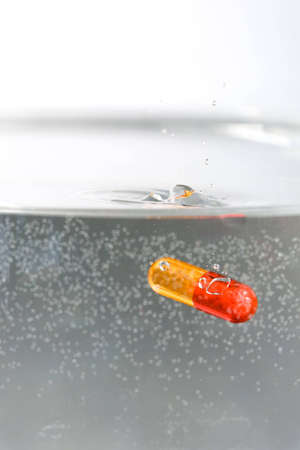 Red and yellow pill dropped in waterの写真素材