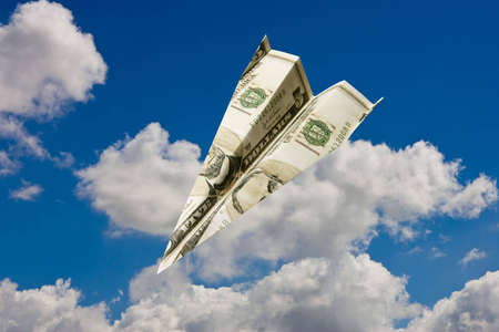 Paper plane made out of dollar notes flying in blue skyの写真素材